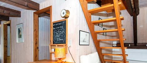 A room with a wooden dresser, a white chair, a wooden ladder, and a chalkboard with text.