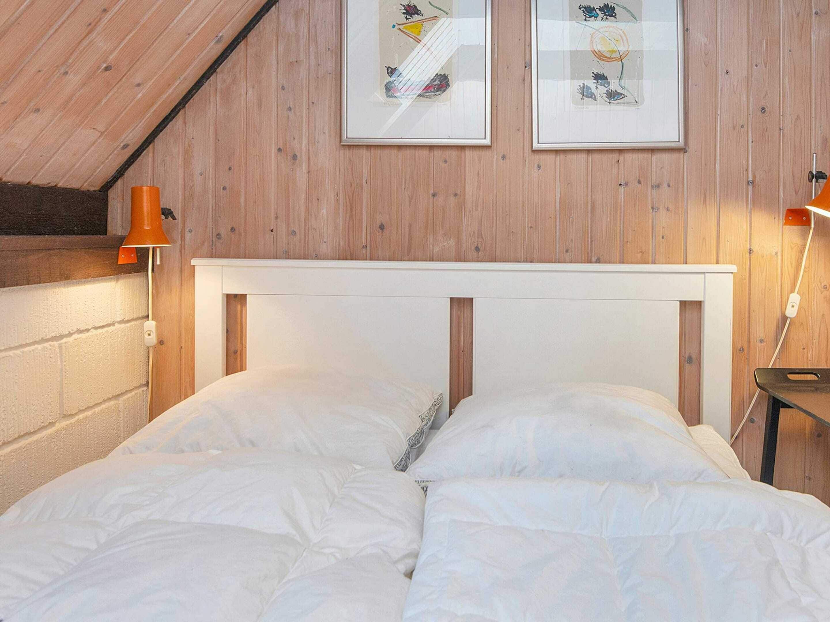 A bedroom with a wooden ceiling, a white headboard, and two framed pictures on the wall.