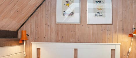 A bedroom with a wooden ceiling, a white headboard, and two framed pictures on the wall.