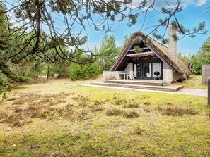 Een landelijk chalet met rieten dak, een overdekte veranda en een klein terras.
