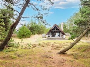 A cabin with a thatched roof, surrounded by trees and a grassy area.