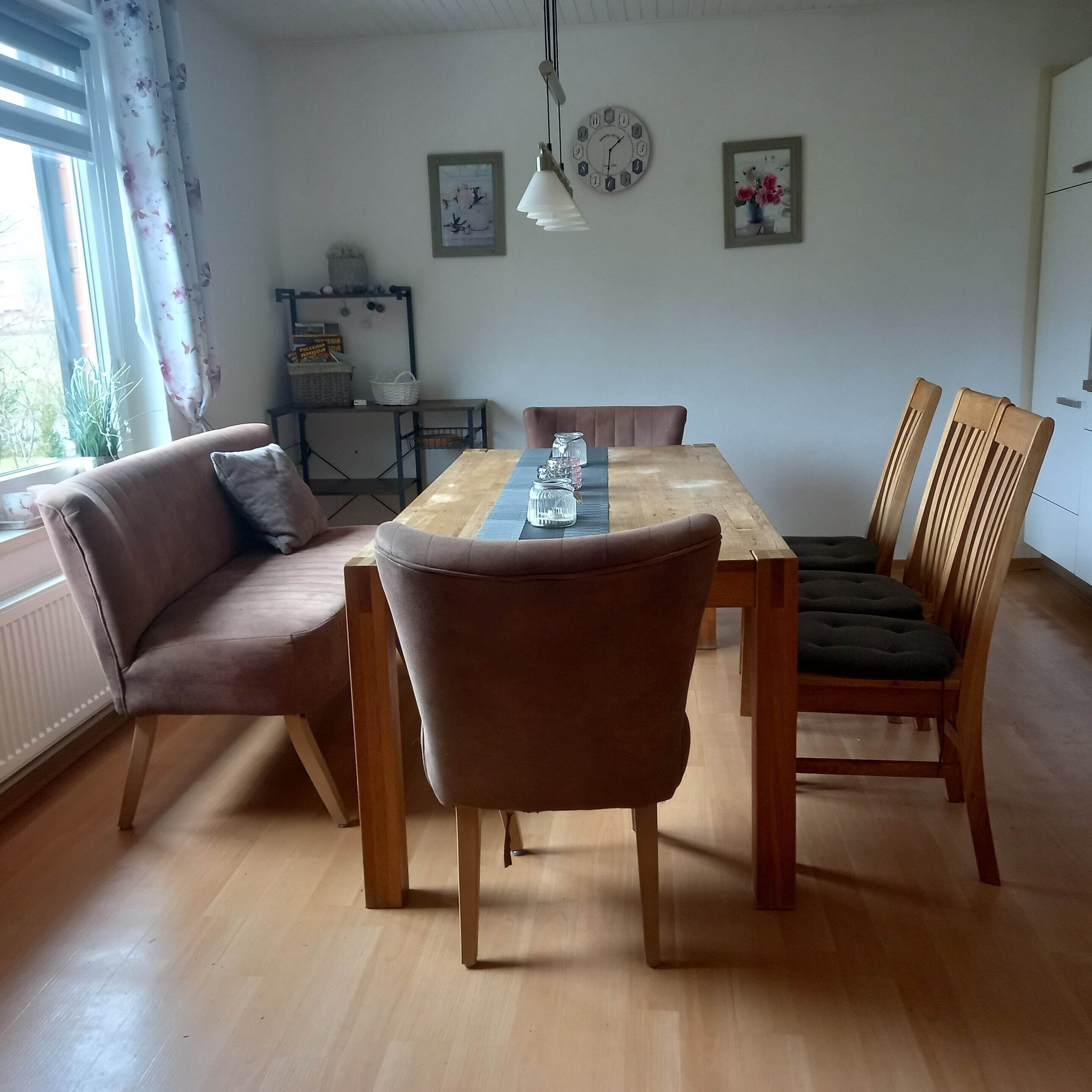 Un coin repas comprenant une table en bois, des chaises rembourrées, un canapé et une fenêtre avec des rideaux.