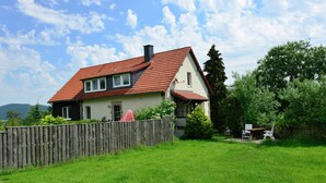 Una casa de dues plantes amb teulada de rajola vermella, una tanca de fusta i un pati amb gespa.