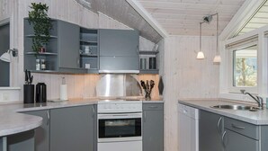 A modern kitchen with grey cabinets, a stainless steel range hood, a built-in oven, and a dishwasher. There is a window providing natural light and a plant on the countertop. - 4 Star Holiday Home in Ebeltoft (Ebeltoft)