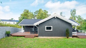 Ein modernes Haus mit grauer Fassade, einem kleinen Fenster und einer Terrasse mit Gartenmöbeln.