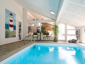 Une piscine intérieure donnant sur un espace repas et ornée d’un tableau représentant un phare.
