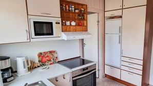 Cozinha compacta equipada com micro-ondas, forno e frigorífico. Há um suporte de madeira para temperos sobre o micro-ondas e uma máquina de café na bancada.