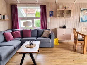 Una sala de estar con un sofá seccional gris, una mesa de centro de madera y un comedor con mesa y sillas de madera.