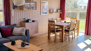 Quarto aconchegante com sofá, mesa de jantar com cadeiras, área de cozinha e vista para o exterior.