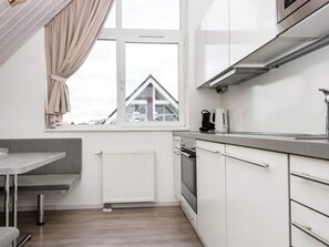 A compact kitchen with a window, a radiator, a stove, and a table with a bench.