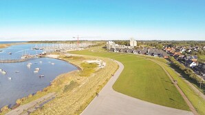 An aerial view of a coastal area with a marina, grassy pathways, and residential buildings. - Holiday Home in Wendtorf (Wendtorf)