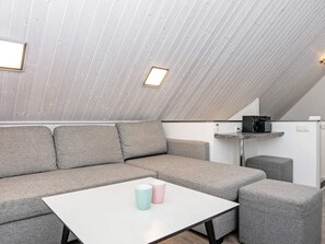 A modern loft-style room with a sectional sofa, a small table, and a kitchenette area.