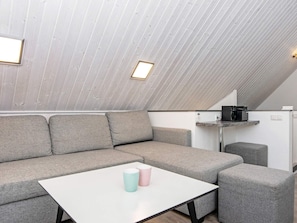 A modern loft bedroom with a sloped ceiling, a sectional sofa, a small table, and a kitchenette area. - Holiday Home in Wendtorf (Wendtorf)