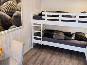 Een stapelbed met een wit frame, grijs beddengoed en een spiegel aan de muur.