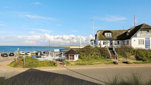 Um hotel à beira-mar com telhado de palha, uma construção adjacente e vista para o mar.