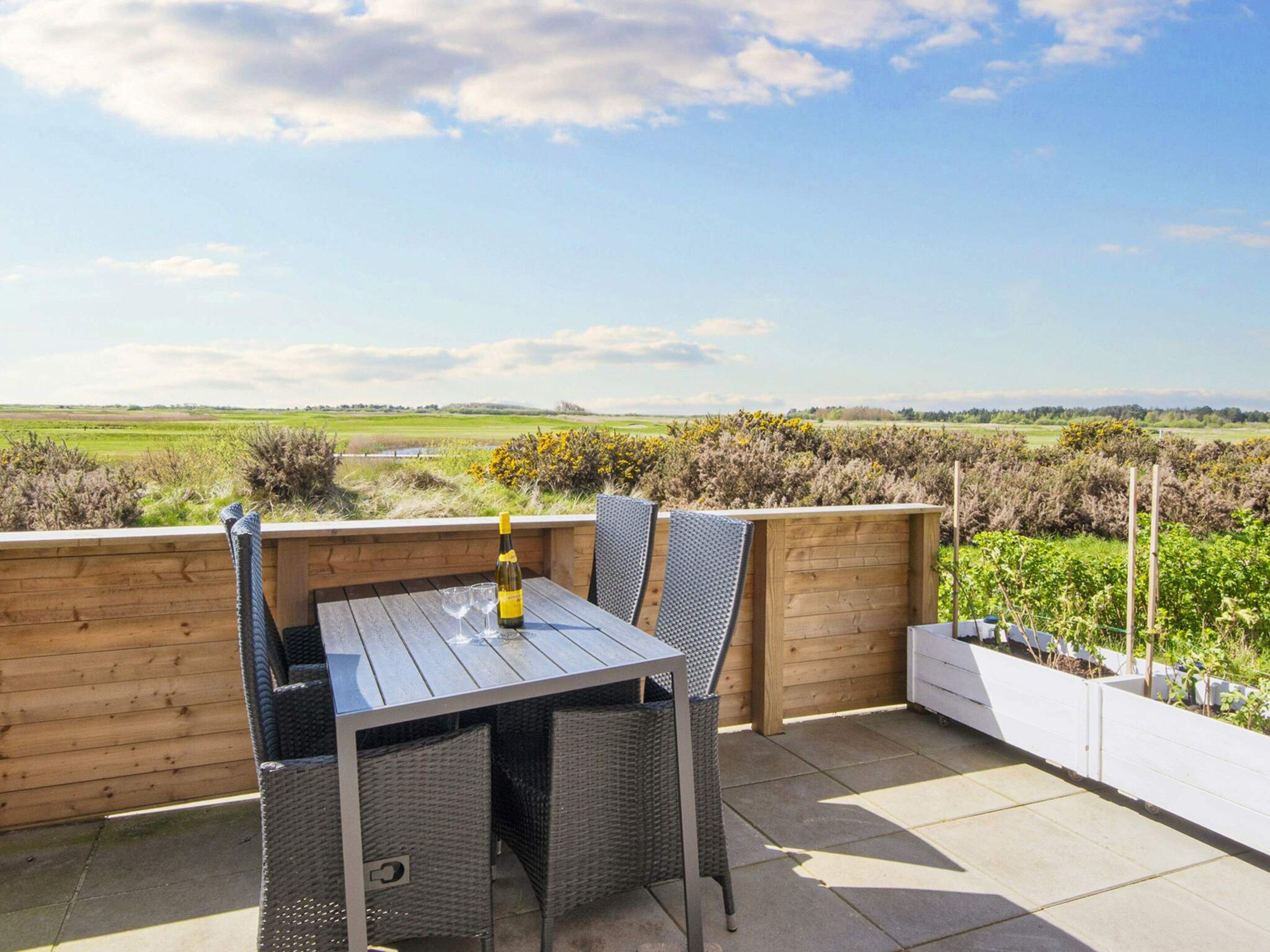 A patio with a table and chairs, a bottle of wine, and a view of a green landscape.