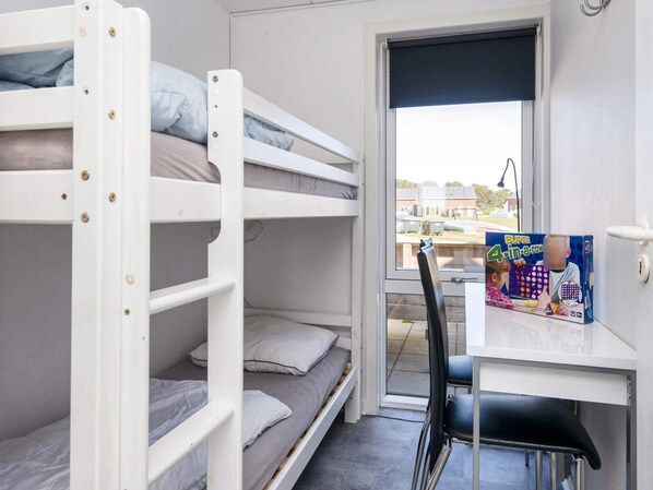 A bunk bed room with a desk and chair, a window with a view of buildings, and a book on the desk.