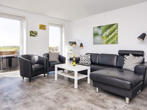 A modern living room with a sofa, armchairs, a coffee table, and a dining area with a table and chairs.