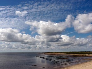 A coastal landscape with a sandy beach, calm water, and a wooden pier extending into the sea.