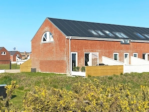 A red brick building with a sloped roof, large windows, and a wooden fence in front.