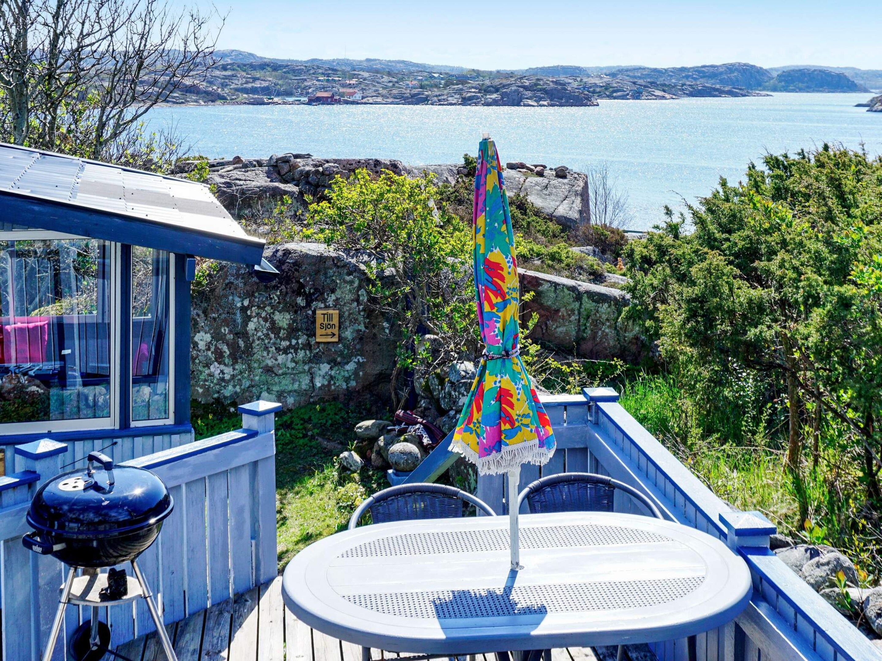Une terrasse dotée d’un barbecue, d’une table et d’un parasol, offrant une vue sur une étendue d’eau et un paysage rocheux.