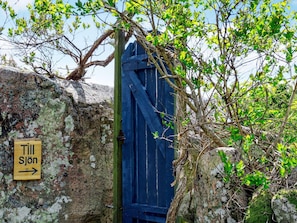 A rustic wooden door with a sign reading "Till Sjön" pointing to the right, surrounded by moss-covered rocks and green foliage. - 4 Person Holiday Home in Hamburgsund (Hamburgsund)