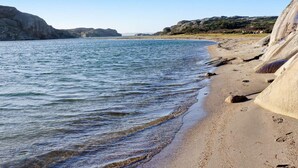 Een kuststrand met helder water, rotskliffen en een zandrijk strand.