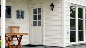 A white building with a covered porch, a wooden table, and two chairs. - Holiday Home in tau (Strand)