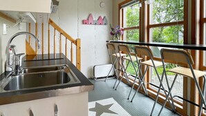 A kitchen with a sink, wooden railing, and a window with a view of greenery. - Holiday Home in tau (Strand)