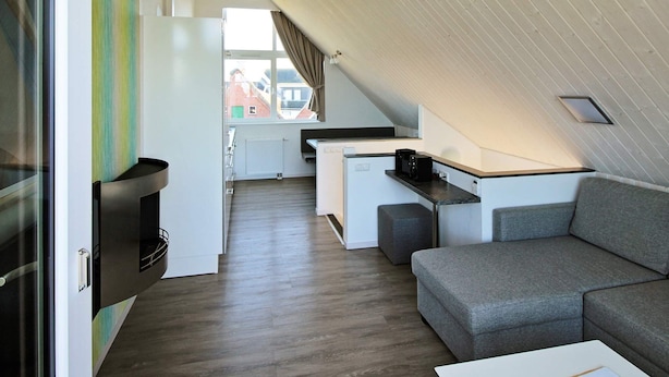 A compact living space with a kitchenette, a gray sofa, and a view through a glass door. - Holiday Home in Wendtorf (Wendtorf)