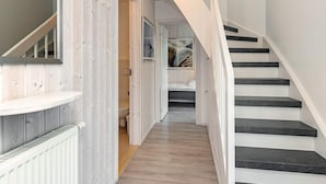 A hallway with a wooden floor, a white staircase with black steps, and a door leading to a bathroom. - Holiday Home in Wendtorf (Wendtorf)