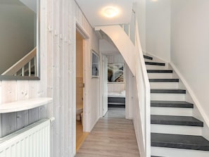 A hallway with a wooden floor, a white staircase with black steps, and a door leading to a bathroom. - Holiday Home in Wendtorf (Wendtorf)