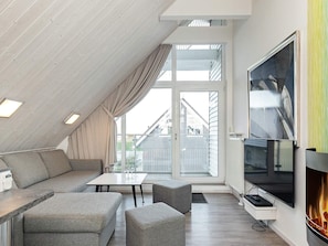 A modern loft bedroom with a sloped ceiling, large windows, a flat-screen TV, and a fireplace. - Holiday Home in Wendtorf (Wendtorf)