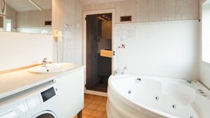 A bathroom with a sink, a washing machine, a bathtub, and a mirror. - Holiday Home in Groemitz (Groemitz)
