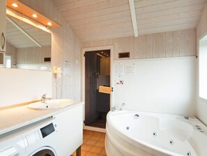 A bathroom with a sink, a washing machine, a bathtub, and a mirror. - Holiday Home in Groemitz (Groemitz)