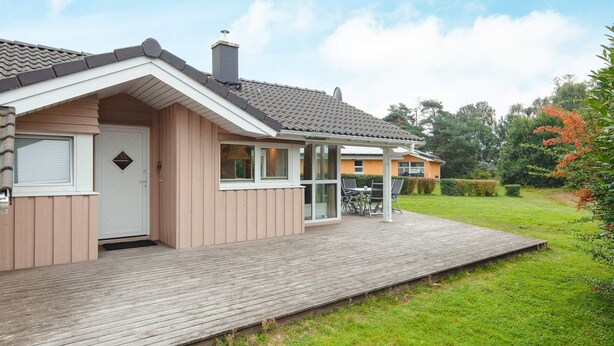 A single-story house with a wooden deck, a covered patio, and a well-maintained lawn. - Holiday Home in Groemitz (Groemitz)