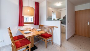 Uma sala de jantar com mesa de madeira, cadeiras estofadas vermelhas, um banco e um candeeiro pendente.