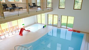 Piscina interior com trampolim, área rasa separada e varanda com assentos.