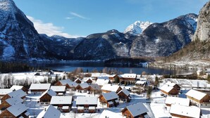 Uma vila coberta de neve com casas de madeira, um lago e montanhas ao fundo.