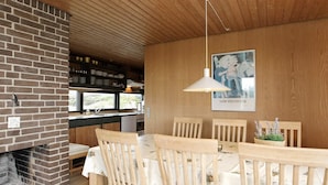 En matplats med en tegelbeklädd öppen spis, trästolar, ett bord täckt med ett vitt bordsduks och en hängande lampa.