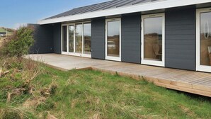 Ett modernt hus med en mörk fasad, stora skjutbara glasdörrar och en träaltan.