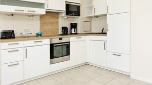 Una cocina moderna con armarios blancos, horno empotrado, microondas y cafetera.