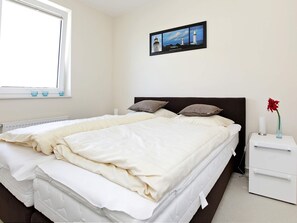 Ein Schlafzimmer mit einem Bett, Kissen, einem Nachttisch, einer Vase mit einer Blume und einem gerahmten Bild an der Wand.