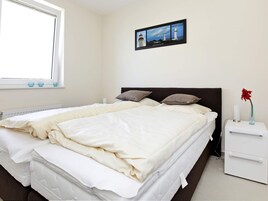 A bedroom with a bed, pillows, a nightstand, a vase with a flower, and a framed picture on the wall.