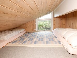 A small attic bedroom with two beds, a window, and a patterned rug.