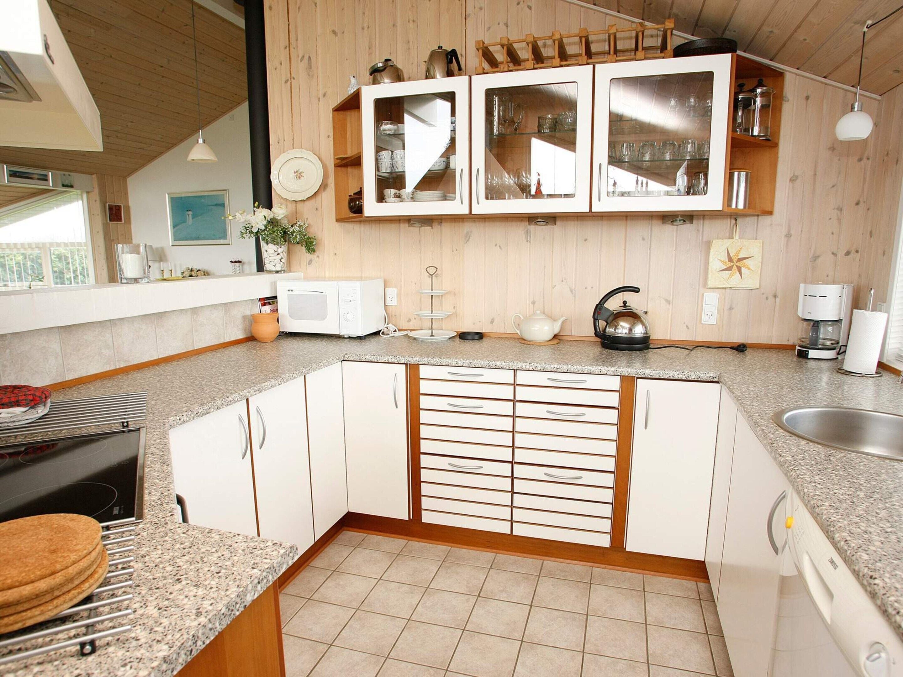 A kitchen with a microwave, kettle, and coffee maker on the countertop, wooden cabinets, and a window with a view.