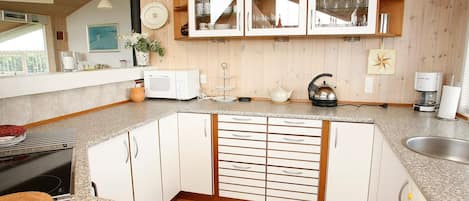Una cocina con microondas, hervidor de agua y cafetera sobre la encimera, armarios de madera y una ventana con vistas.