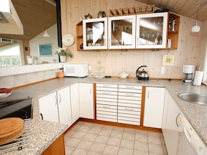 A kitchen with a microwave, kettle, and coffee maker on the countertop, wooden cabinets, and a window with a view.