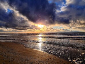 A beach with waves, a sunset, and a cloudy sky.