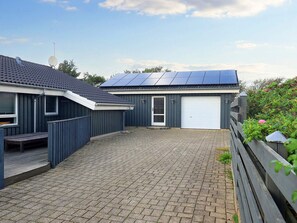 A residential property with a paved driveway, a covered outdoor seating area, a garage, and solar panels on the roof.
